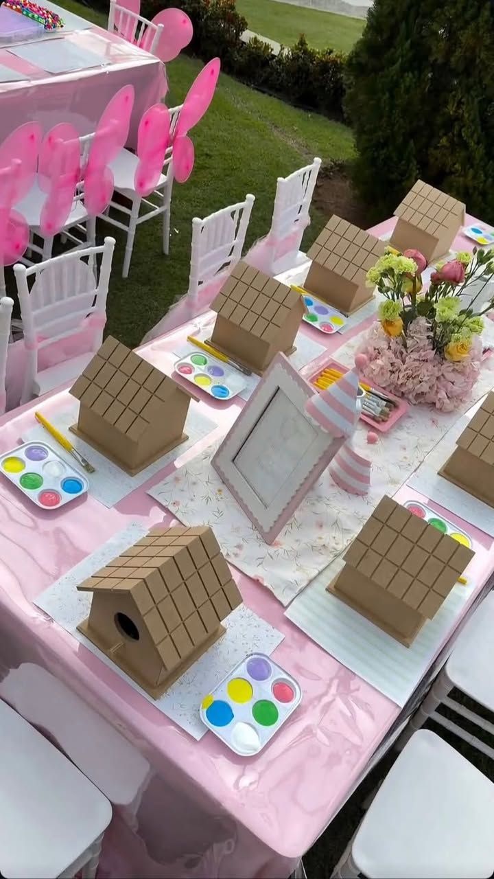 Mesa de festa decorada em rosa com casinhas de madeira e paletas de tinta para as crianças pintarem
