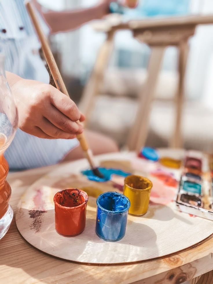 Criança pintando com pincel e potes de tinta